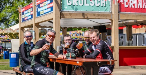Vijf wielrenners in wielerkleding zitten aan een picknicktafel en genieten van een biertje bij een Grolsch-bar.