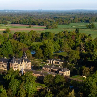 Luchtfoto van een historisch kasteel omringd door groene bossen en velden in een landelijke omgeving.
