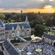 Aerial view of a concert at sunset outside a historic castle, with audience seated and lush trees around.