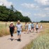Groep mensen wandelt op een landelijk pad omringd door groene velden en bomen onder een bewolkte lucht.
