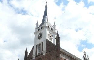 Foto van een historische kerk met kloktoren en bakstenen gevel onder een gedeeltelijk bewolkte lucht.