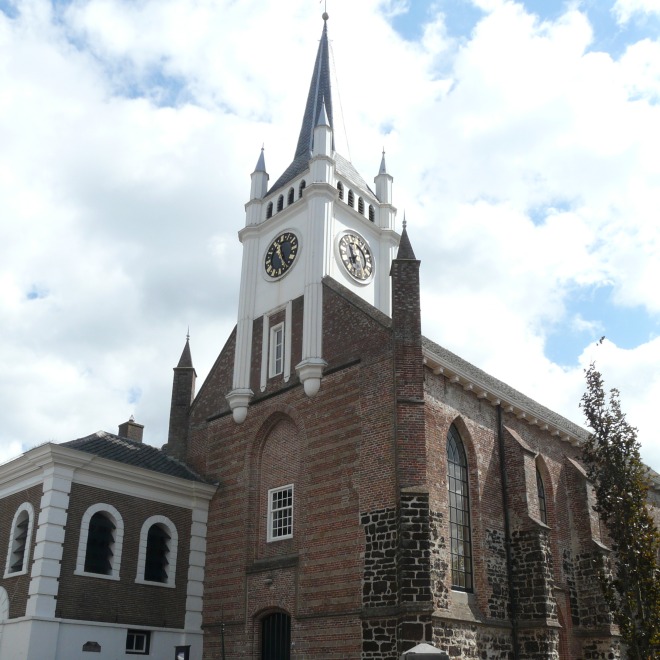 Foto van een historische kerk met kloktoren en bakstenen gevel onder een gedeeltelijk bewolkte lucht.
