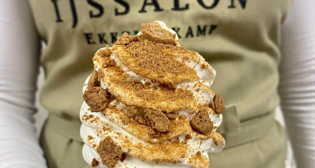 Softeis in einer Waffel, garniert mit Spekulatiusstückchen, gehalten von einer Person mit Schürze.