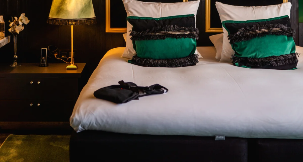 Stijlvolle slaapkamer met donkergroene muren, moderne verlichting, tweepersoonsbed en luxe kussens.