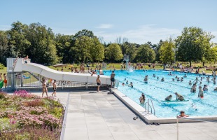 Buiten zwembad met glijbaan, veel mensen genieten van zwemmen en zonnen op een zonnige dag.
