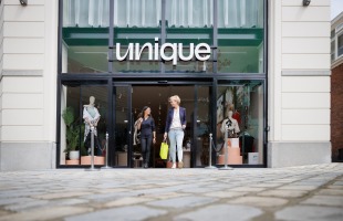 Twee vrouwen verlaten samen een kledingwinkel genaamd Unique met een winkeltas in de hand.