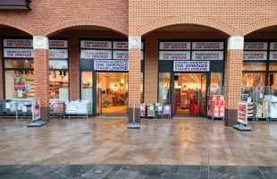 Vooraanzicht van een parfumerie en medicijnwinkel met open deuren, winkelwagens en producten buiten.