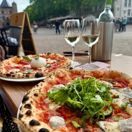 Twee authentieke pizza's met witte wijn op een terras met uitzicht op een sfeervol stadsplein.