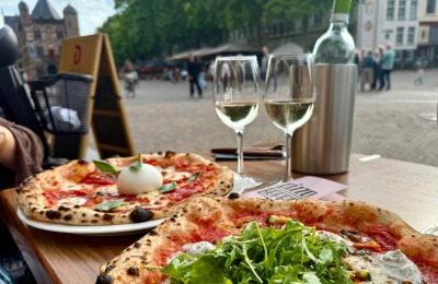 Twee authentieke pizza's met witte wijn op een terras met uitzicht op een sfeervol stadsplein.