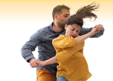 Twee mensen dansen expressief samen, waarbij de vrouw een gele blouse draagt en de man een blauwe overhemd.