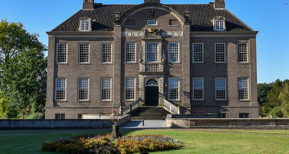 Vorderansicht eines historischen niederländischen Herrenhauses mit großen Fenstern und Garten bei Sonne.
