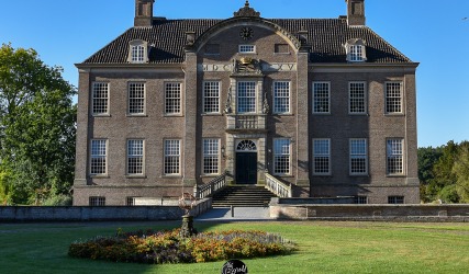 Vorderansicht eines historischen niederländischen Herrenhauses mit großen Fenstern und Garten bei Sonne.