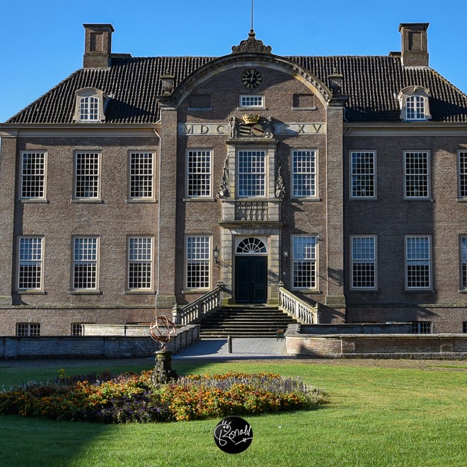 Vooraanzicht van een historisch Nederlands landhuis met grote ramen en tuin op een zonnige dag.