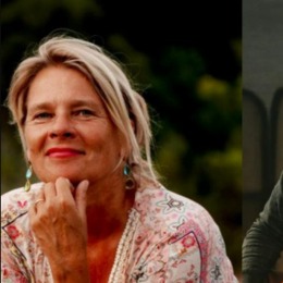 Twee mensen, een vrouw met blond haar en een man met donker haar en baard, glimlachen naar de camera.