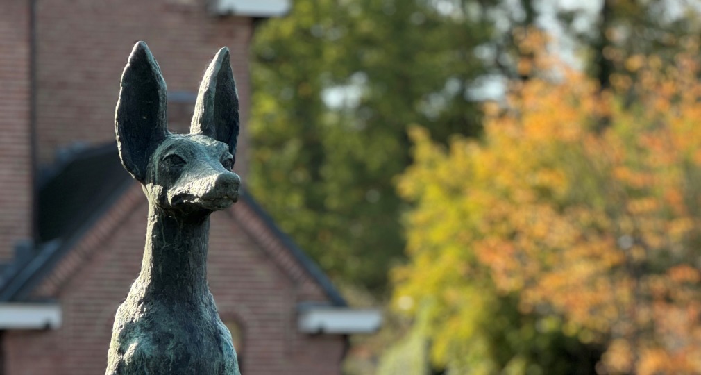 Een standbeeld van een mythische hond, genaamd Helhond, met een informatiebord op een stenen sokkel.