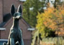 A statue of a mythical dog called Helhound, with an information plaque on a brick pedestal outdoors.