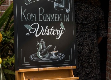 Willkommensschild am Eingang mit Text 'Willkommen Kommen Sie herein in die Vilsterij' und Zeichnung einer Kaffeekanne und Tasse.