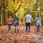 Gezin wandelt samen door een kleurrijk herfstbos, kinderen spelen en ouders houden handen vast.