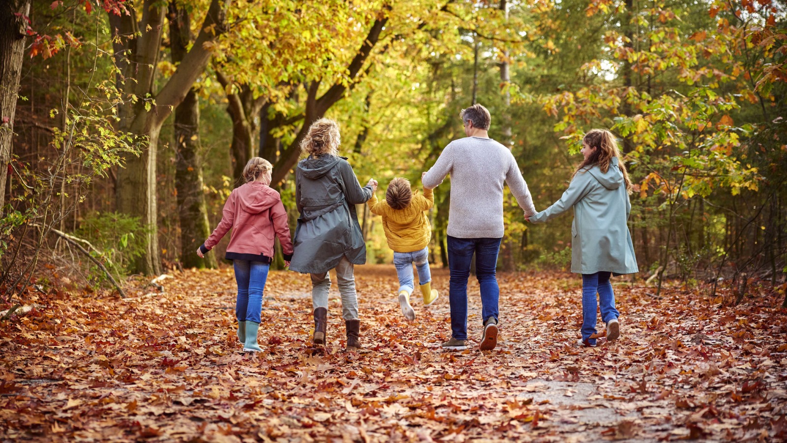 Gezin wandelt samen door een kleurrijk herfstbos, kinderen spelen en ouders houden handen vast.