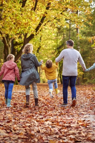 Gezin wandelt samen door een kleurrijk herfstbos, kinderen spelen en ouders houden handen vast.