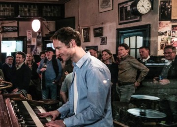 Een jazzband treedt op in een gezellige bar terwijl een geïnteresseerd publiek aandachtig toekijkt.