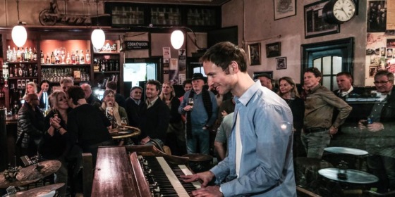 Een jazzband treedt op in een gezellige bar terwijl een geïnteresseerd publiek aandachtig toekijkt.
