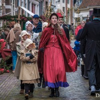 Groep mensen in Dickens-kostuums loopt door een sfeervolle straat tijdens het Dickens Festijn.