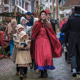 Groep mensen in Dickens-kostuums loopt door een sfeervolle straat tijdens het Dickens Festijn.