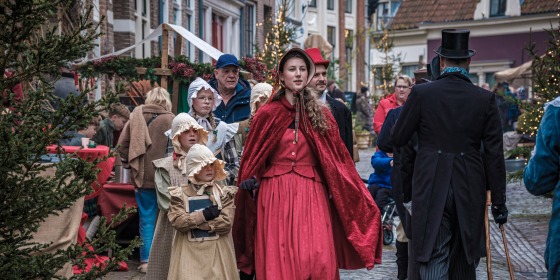 Groep mensen in Dickens-kostuums loopt door een sfeervolle straat tijdens het Dickens Festijn.