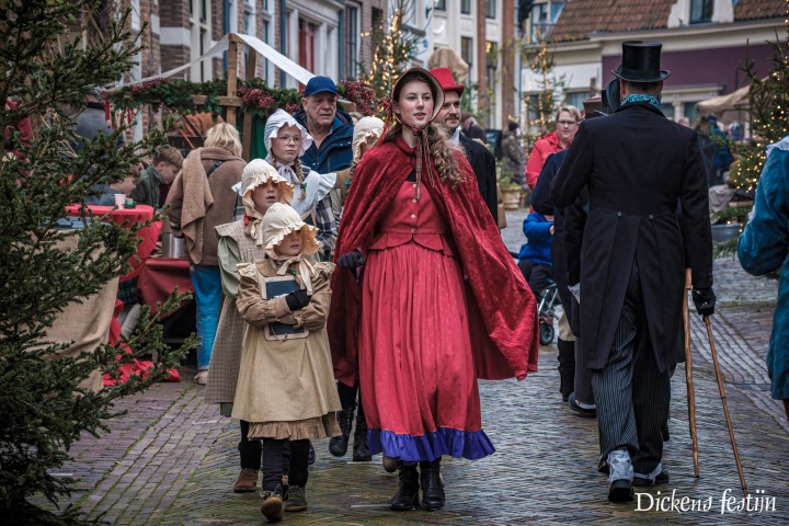 Groep mensen in Dickens-kostuums loopt door een sfeervolle straat tijdens het Dickens Festijn.
