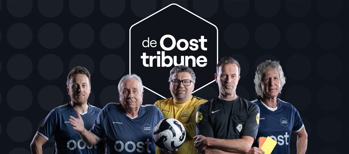 Vijf mannen in voetbaloutfits en scheidsrechter bij de Oost Tribune, met een voetbal en gele kaart.