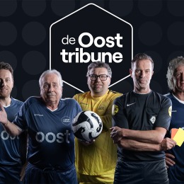 Vijf mannen in voetbaloutfits en scheidsrechter bij de Oost Tribune, met een voetbal en gele kaart.