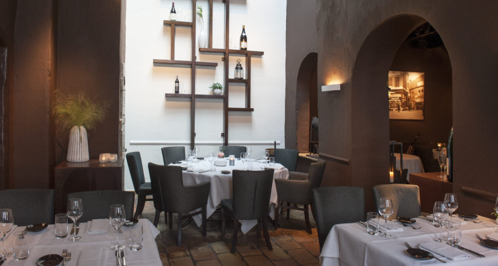 Een elegant restaurantinterieur met ronde en vierkante tafels, witte tafelkleden en moderne decoratie.