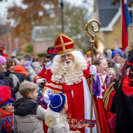 Sinterklaas arriveert te midden van een feestelijke menigte in Nederland, omringd door blije kinderen.