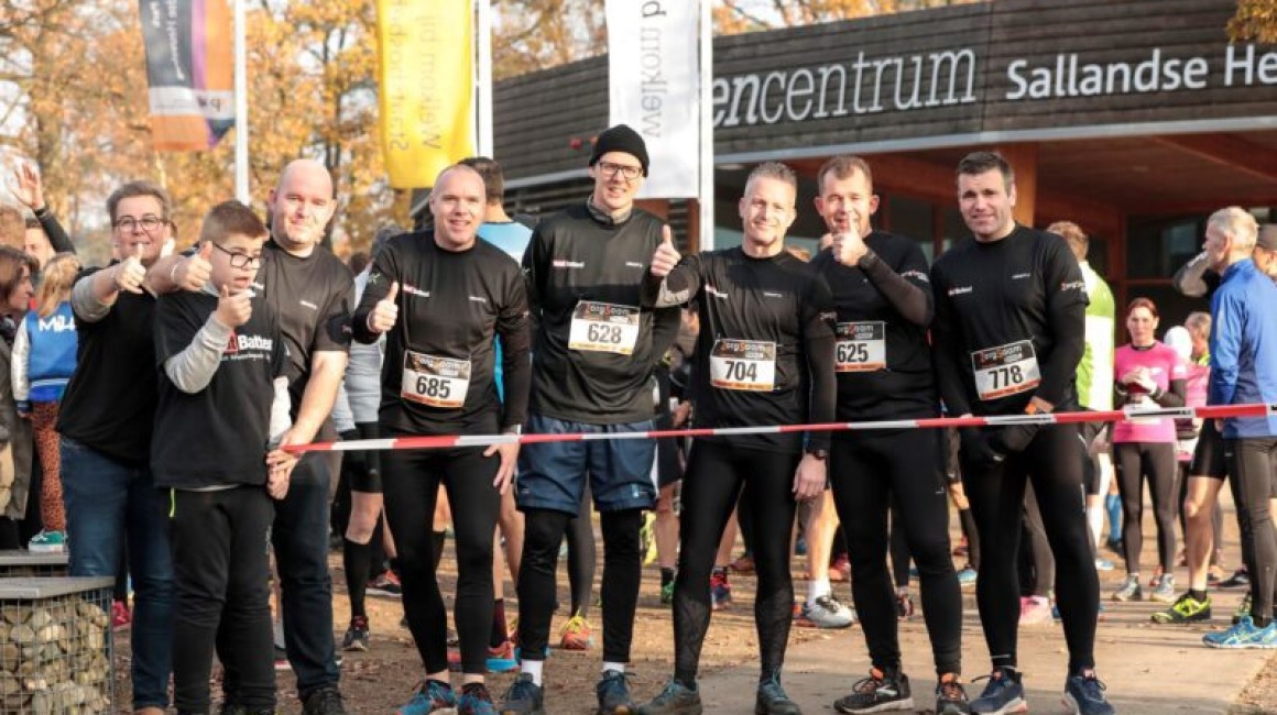 Groep hardlopers poseert lachend bij startlijn tijdens sportevenement bij het bezoekerscentrum.