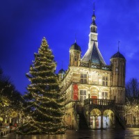 Verlichte kerstboom en historische gebouwen op een sfeervol avondplein in Nederland tijdens kersttijd.