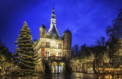 Verlichte kerstboom en historische gebouwen op een sfeervol avondplein in Nederland tijdens kersttijd.