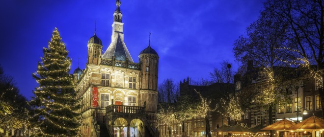 Verlichte kerstboom en historische gebouwen op een sfeervol avondplein in Nederland tijdens kersttijd.
