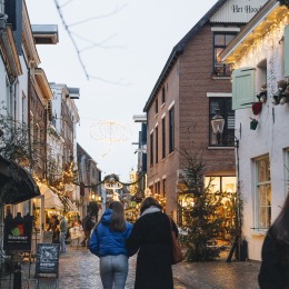 Sfeervol verlichte winkelstraat in Nederland tijdens de feestdagen met mensen die wandelen in de avond.