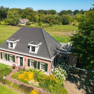Luchtfoto van een traditioneel Nederlands huis met zwart dak, omgeven door groene weiden en tuinen.