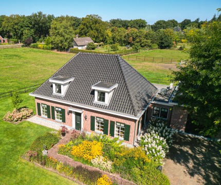 Luchtfoto van een traditioneel Nederlands huis met zwart dak, omgeven door groene weiden en tuinen.