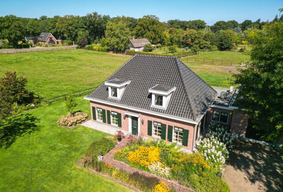 Luchtfoto van een traditioneel Nederlands huis met zwart dak, omgeven door groene weiden en tuinen.