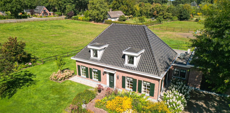 Luchtfoto van een traditioneel Nederlands huis met zwart dak, omgeven door groene weiden en tuinen.