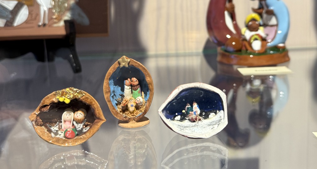Kleine en grote kerststalfiguren tentoongesteld in een vitrine, met kleurrijke en miniatuurontwerpen.