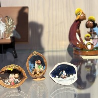 Kleine en grote kerststalfiguren tentoongesteld in een vitrine, met kleurrijke en miniatuurontwerpen.