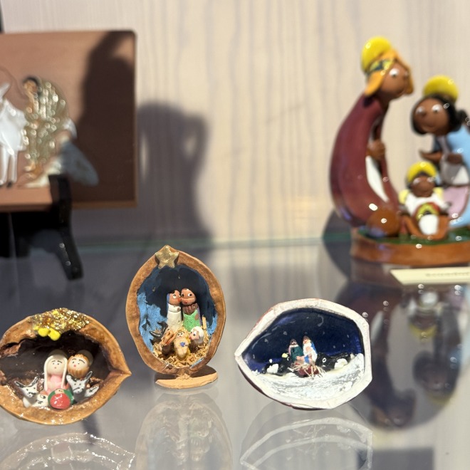 Kleine en grote kerststalfiguren tentoongesteld in een vitrine, met kleurrijke en miniatuurontwerpen.