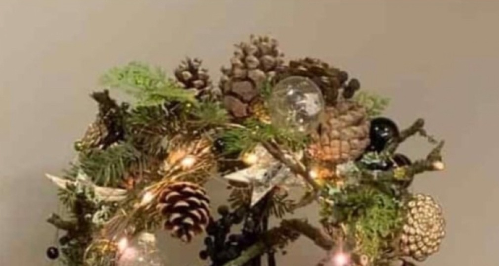 Decoratief kerstobject met dennentakken, dennenappels, kerstballen en verlichting op staande standaard.