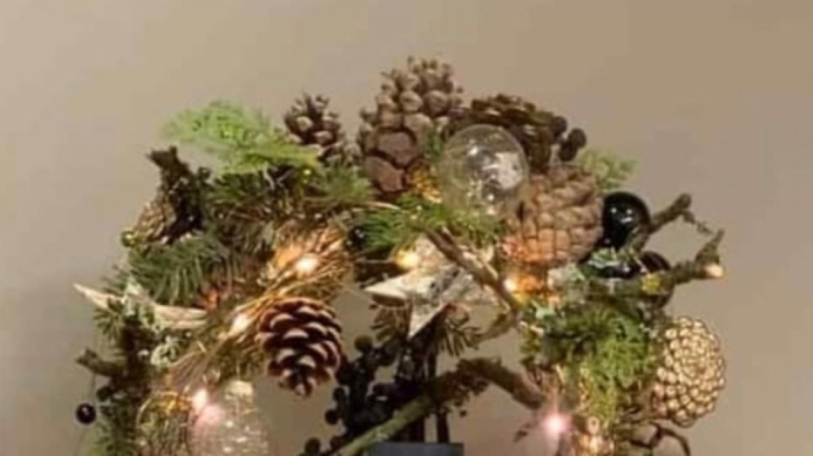 Festive Christmas decoration featuring pine branches, cones, ornaments, and lights on a standing base.