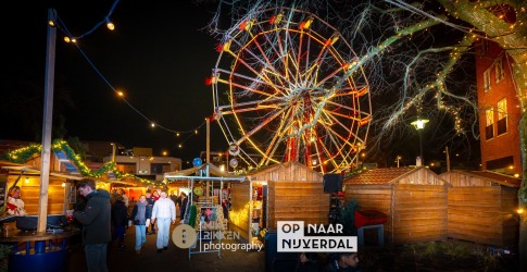 Gezellige kerstmarkt in Nijverdal met verlichte kermisattracties, houten kraampjes en bezoekers 's avonds.