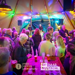Mensen genieten van live muziek en drankjes in een kleurrijke tent tijdens een gezellig evenement.